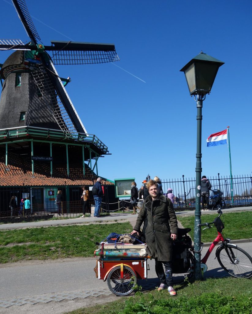 Maarten Vetart Vet standing in front of a windmill. The sky is clear and a Dutch flag ripples in the wind.